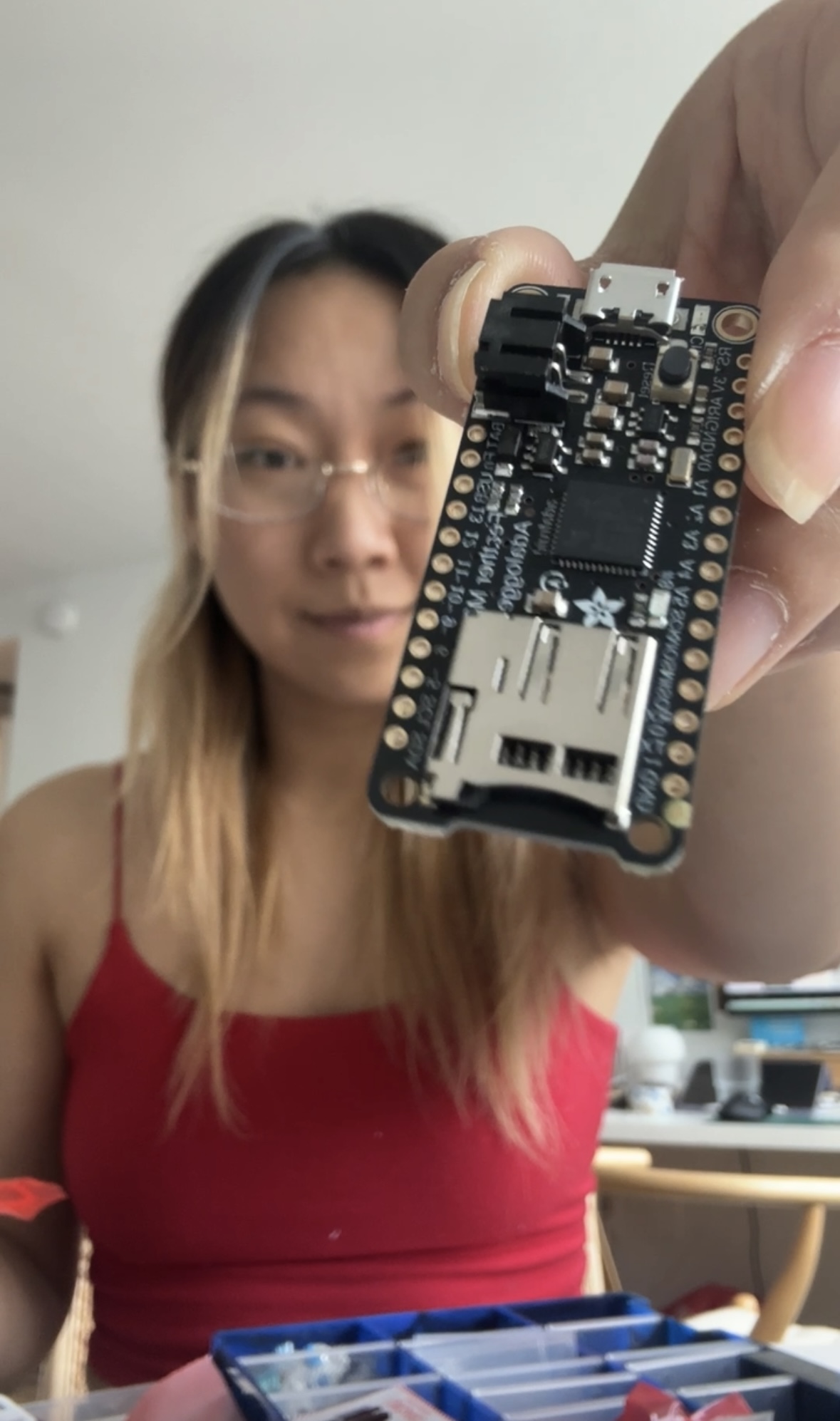 Ling holding an Adafruit Feather microcontroller board up to the camera.